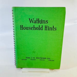 May include: A bright green spiral-bound book titled Watkins Household Hints in black text. The cover includes the company name The J. R. Watkins Co. and the city locations Newark, Memphis, Winona, and Oakland printed in black at the bottom.