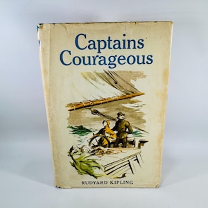 May include: Vintage hardcover book titled "Captains Courageous" by Rudyard Kipling. The cover features an illustration of a sailboat with two figures on deck. The book has a worn, aged appearance.