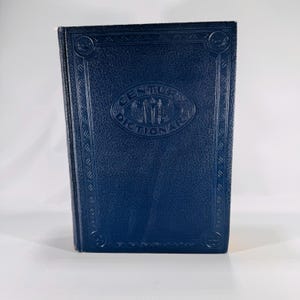 May include: A navy blue hardcover book titled "Century Dictionary". The cover has an embossed design with the title in an oval shape. The book is standing upright against a white background.