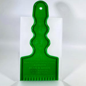 May include: A bright green plastic garden tool with a wavy handle and a flat, toothed edge. The tool has the text "From Your 'All Weather' Friends AUBURN BEAN & GRAIN" and a phone number printed on it.
