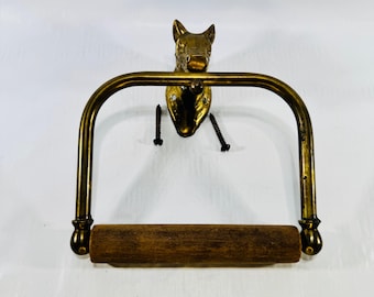 Può includere: Un portarotolo in ottone con supporto a parete a forma di testa di cavallo, un braccio in metallo curvo e un rullo cilindrico in legno. Due viti in metallo nero sono posizionate vicino al supporto per l'installazione.