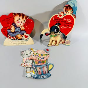 May include: Three vintage Valentine's Day cards featuring cartoon animals. One card shows a kitten with a heart, another a puppy with a heart, and the third a cat with a cup of whipped cream. Each card has a unique message.