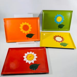 May include: Four rectangular trays in bright colors: orange, green, yellow, and red. Each tray features a sunflower design with a green leaf. The sunflowers have yellow, white, and orange petals with a yellow or orange center.