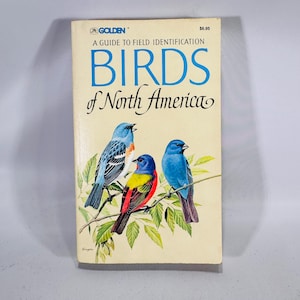 May include: A vintage book titled "Birds of North America" with a cream-colored cover. The cover features illustrations of three colorful birds perched on a branch. The book is a guide to field identification.