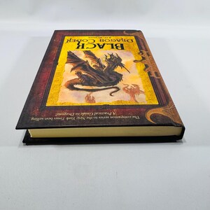 May include: A hardback book titled "Black Dragon Codex" featuring a dragon illustration on the cover. The cover has a yellow background with a black dragon and text. The book is part of a series and is a practical guide to dragons.