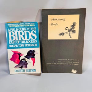May include: Two vintage books on a white surface. The book on the left is titled "A Field Guide to the Birds East of the Rockies" by Roger Tory Peterson, with bird illustrations. The book on the right is titled "Attracting Birds".