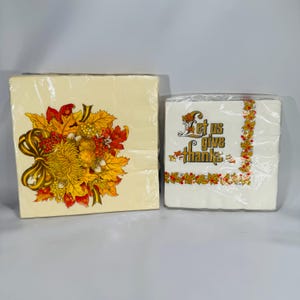 May include: Two packages of paper napkins. One package has a floral design with autumn leaves and a bow. The other package has the text "Let us give thanks" with autumn leaf accents. Both are wrapped in clear plastic.
