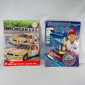 May include: Two vintage NASCAR race programs. The left program features two yellow Miller High Life race cars at Michigan U.S.A. on June 26, 1988. The right program displays the Daytona 500 from February 19, 1989, with a driver, a trophy, and a red race car.