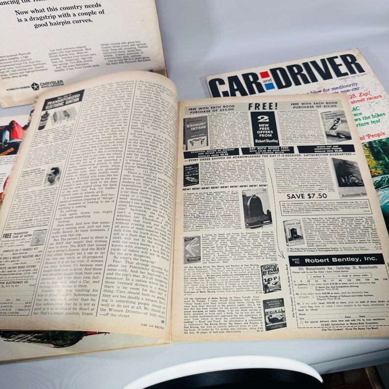May include: An open vintage magazine, titled "Car and Driver," with yellowed pages. The text is in black, and there are various articles and advertisements. The magazine is open to a spread with text and images.