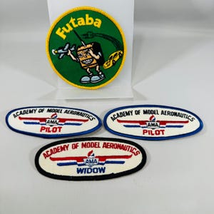 May include: A circular Futaba patch with a green background, yellow border, and a cartoon character holding a model airplane. Below are three oval Academy of Model Aeronautics patches with white backgrounds, two labeled Pilot and one labeled Widow.
