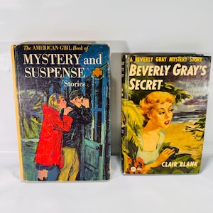 May include: Two vintage books with colorful covers. One is titled "The American Girl Book of Mystery and Suspense" with a red-coated girl and man. The other is "Beverly Gray's Secret" with a woman on a beach. Both books are in good condition.