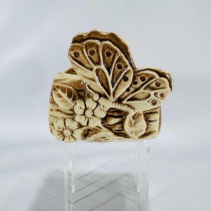 May include: A ceramic butterfly-shaped planter in shades of beige and brown. The planter features a detailed butterfly design with floral and leaf accents. The wings of the butterfly are raised and textured, adding depth to the design.