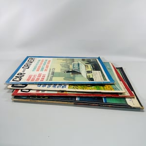 May include: A pile of vintage "Car and Driver" magazines. The top magazine shows a car on the cover with the text "BMW 2000 CS". The magazines have a blue, red, and black colour scheme.