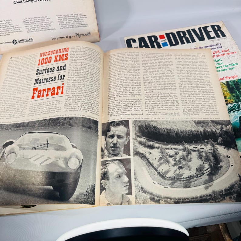 May include: An open magazine with a car racing article. The headline reads "N&uuml;rburgring 1000 KMS Surtees and Mairesse for Ferrari." The article includes images of a race car, driver portraits, and a track. The magazine is "Car and Driver."