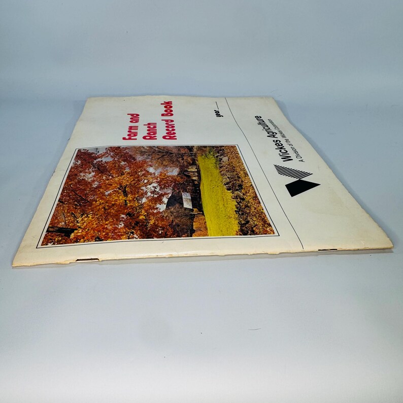 Pu&ograve; includere: Un vecchio "Farm and Ranch Record Book" con una foto di paesaggio di una fattoria. La copertina presenta il testo "Farm and Ranch Record Book" in rosso, con il logo "Wickes Agriculture" sul lato destro.