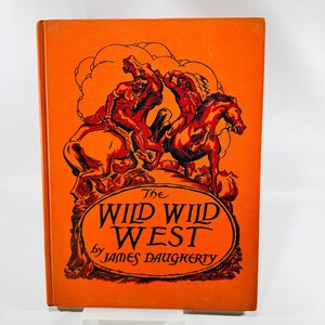 May include: A hardcover book with a bright orange cover featuring black line art of two figures riding horses. The title The Wild Wild West by James Daugherty is printed in black lettering within an oval frame on the front cover of the book.