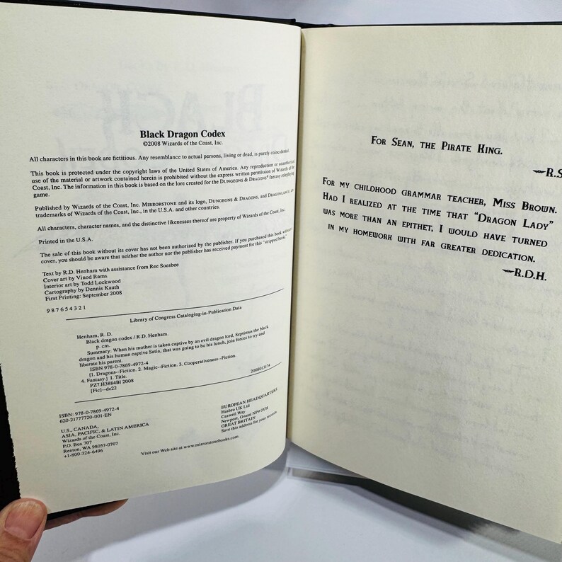 May include: An open book with the title "Black Dragon Codex" and copyright details. The pages are cream-coloured, with black text. The right-hand page features a dedication to Sean, the Pirate King, and Miss Brown.