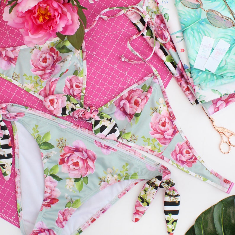 May include: A floral print bikini top and bottom with black and white striped trim. The top has a tie closure at the neck and the bottom has a tie closure at the sides.
