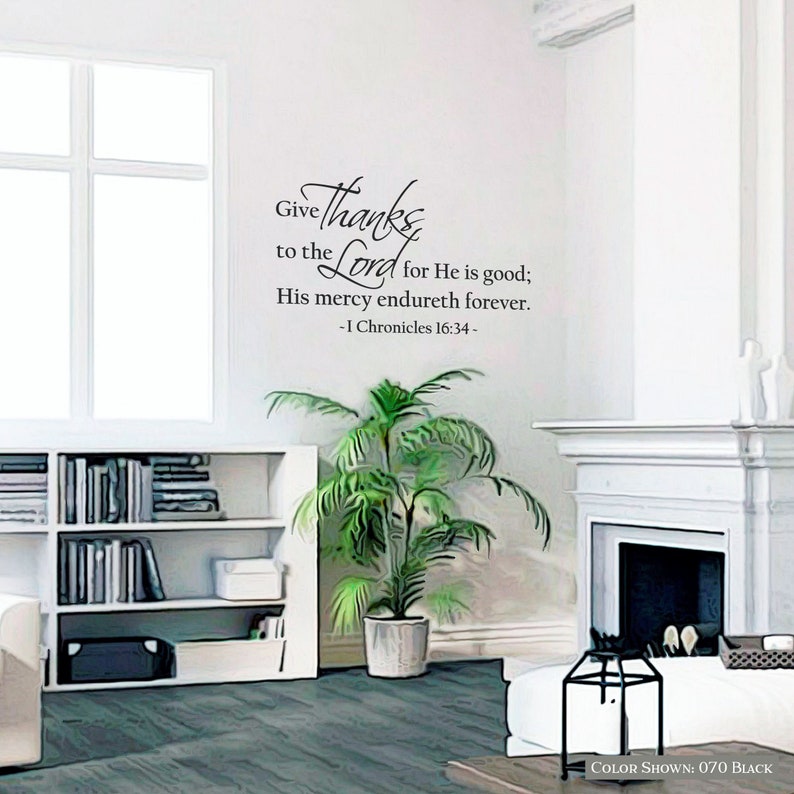 May include: A white wall with a black vinyl decal featuring a bible verse from 1 Chronicles 16:34. The verse reads "Give thanks to the Lord for He is good; His mercy endureth forever." The decal is in a living room setting with a potted plant, a bookshelf, and a fireplace.