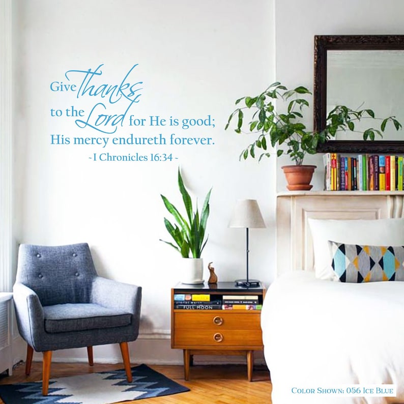 May include: A wall decal with a blue and white design that reads "Give thanks to the Lord for He is good; His mercy endureth forever. - I Chronicles 16:34 -" The decal is shown in a living room setting with a chair, a side table, a bed, and plants.