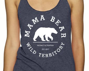 May include: A navy blue tank top with a white graphic of a bear inside a circle. The text around the bear reads "Mama Bear Wild Territory Instinct Activation Est. 2017".