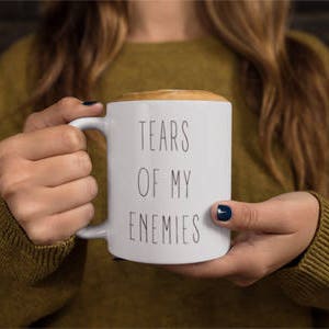 May include: White ceramic coffee mug with black text that reads "Tears of my enemies".