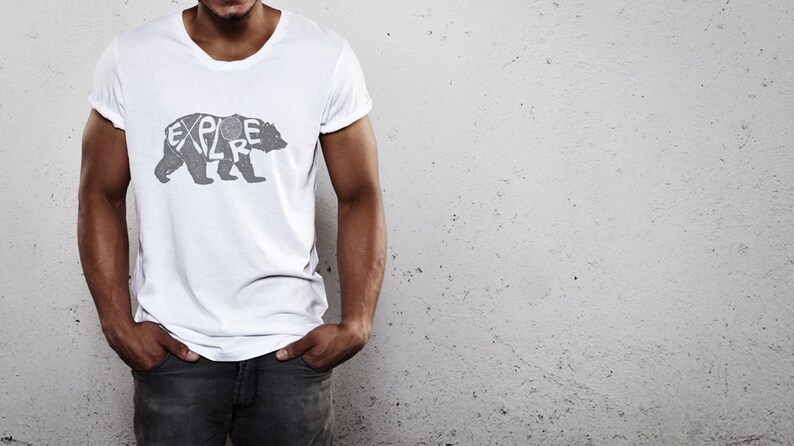 May include: White t-shirt with a gray bear graphic. The word "EXPLORE" is integrated into the bear's silhouette. The shirt has a crew neck and short sleeves.