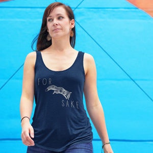 May include: A woman wearing a navy blue tank top with a white graphic of a fox jumping and the text "FOR SAKE".