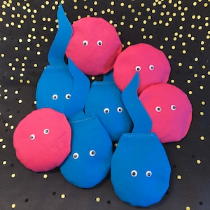 May include: A set of eight bean bags in pink and blue with googly eyes. The bean bags are shaped like teardrops and are arranged in a circle.
