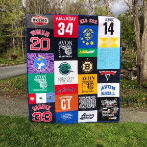 May include: A handmade quilt featuring various sports team logos and jersey designs. The quilt incorporates logos from the Red Sox, Avon Basketball, and Endicott College. The quilt also includes the names Halladay, Youkilis, and Lepage, along with the numbers 34, 20, and 14.