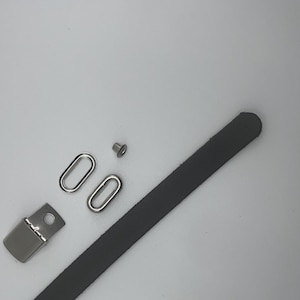 May include: A set of silver-toned hardware for leather crafting, including two oval rings, a small rivet, and a black leather strap.