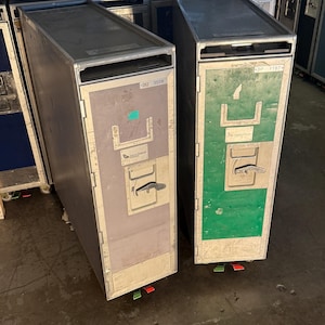 May include: Two silver metal luggage carts with green and grey doors. The cart on the left has the text "DU 3559" on the door. The cart on the right has the text "DP 11874" on the door.