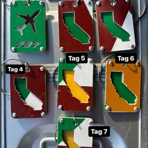 May include: Seven metal tags with different designs. The tags are all rectangular and have a green, white, red, orange, and yellow color scheme. The tags are labeled with the numbers 1 through 7. The tags are attached to a metal surface with a wire. The tags have the text '787' on one of them. The tags are all different sizes and shapes.