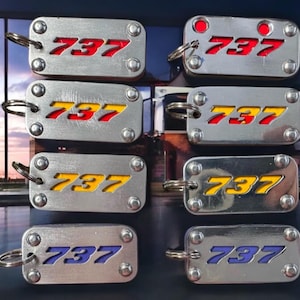 May include: Eight silver keychains with the number 737 embossed on them. The numbers are in different colours: red, yellow, and blue.