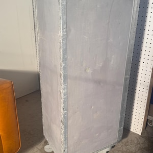 K&ouml;nnte beinhalten: Ein hoher, silberner Metallschrank mit vier R&auml;dern. Der Schrank hat eine rechteckige Form und eine glatte, leicht strukturierte Oberfl&auml;che. Der Schrank steht auf einem Betonboden.