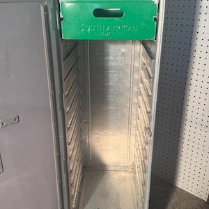 K&ouml;nnte beinhalten: Ein silberner Airline-Cateringwagen mit einer gr&uuml;nen Schublade mit der Aufschrift "South African Airways". Der Wagen hat mehrere Regale und ist mit offener T&uuml;r ge&ouml;ffnet.