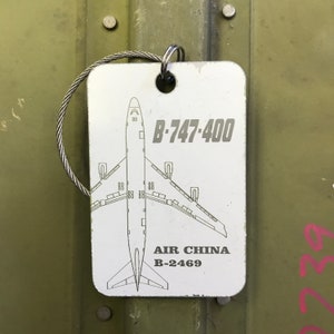 K&ouml;nnte beinhalten: Ein wei&szlig;es Schild mit einer schwarz-wei&szlig;en Umrandung eines Boeing 747-400 Flugzeugs. Das Schild tr&auml;gt den Text "B-747-400" und "AIR CHINA B-2469" aufgedruckt.