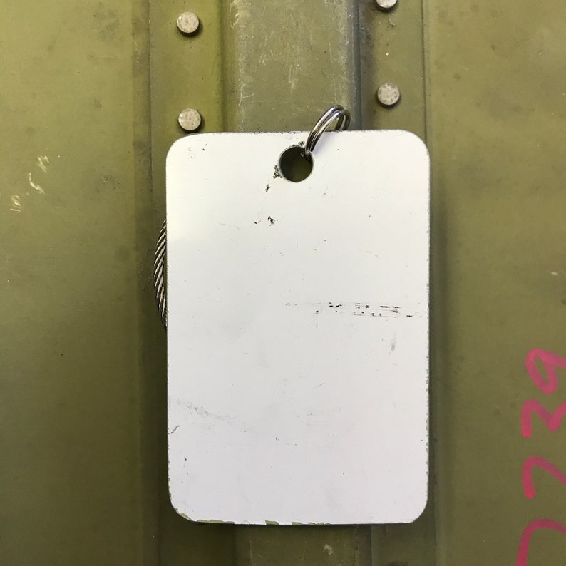 K&ouml;nnte beinhalten: Ein wei&szlig;es rechteckiges Schild mit einem daran befestigten Metallring oben. Das Schild ist leer und hat ein kleines Loch in der Mitte.