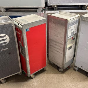 May include: Four industrial metal carts with wheels. One cart has a gray textured front with a white logo and the word "newest". Another cart is red. The other two carts are silver. They appear to be used for storage or transport.
