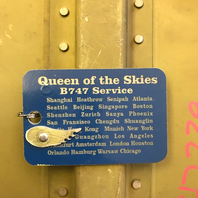 K&ouml;nnte beinhalten: Ein blaues Schild mit dem Text "Queen of the Skies B747 Service" und einer Liste von St&auml;dten, darunter Shanghai, Heathrow, Senipah, Atlanta, Seattle, Peking, Singapur, Boston, Shenzhen, Z&uuml;rich, Sanya, Phoenix, San Francisco, Chengdu, Shuangliu, Hongkong, M&uuml;nchen, New York, Guangzhou, Los Angeles, Frankfurt, Amsterdam, London, Houston, Orlando, Hamburg, Warschau und Chicago.