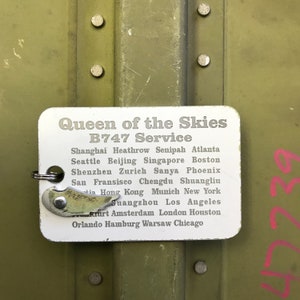 K&ouml;nnte beinhalten: Ein wei&szlig;es Schild mit dem Text "Queen of the Skies B747 Service" und einer Liste von St&auml;dten, darunter Shanghai, Heathrow, Senipah, Atlanta, Seattle, Peking, Singapur, Boston, Shenzhen, Z&uuml;rich, Sanya, Phoenix, San Fransisco, Chengdu, Shuangliu, Hongkong, M&uuml;nchen, New York, Guangzhou, Los Angeles, Amsterdam, London, Houston, Orlando, Hamburg, Warschau und Chicago.