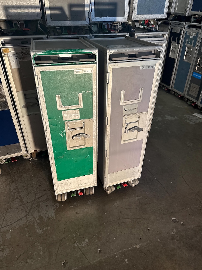 K&ouml;nnte beinhalten: Zwei Metall-Gep&auml;ckwagen mit R&auml;dern. Der Wagen links ist gr&uuml;n und hat den Text "22cm x 33.5cm" auf der Vorderseite. Der Wagen rechts ist grau und hat den Text "DU-4596" auf der Vorderseite.