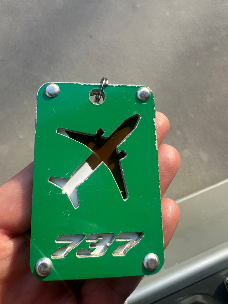 May include: A green metal keychain with a white airplane cutout and the number 737 in white lettering.