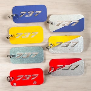 May include: Six keychains with the number 737 cut out of the metal. The keychains are in different colors, including blue, yellow, silver, and red.