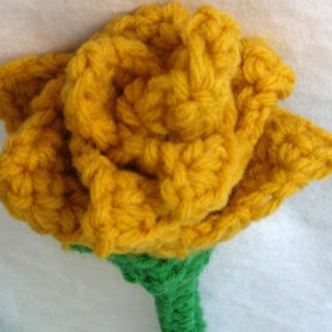 May include: A crocheted yellow rose with a green stem. The rose is made with a textured yarn and has a realistic appearance.