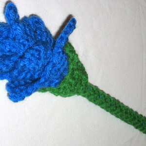 May include: A crocheted flower with a blue flower head and a green stem.