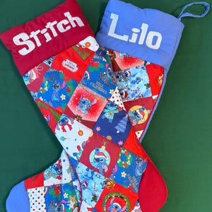 Puede incluir: Dos calcetines navideños con diseños de patchwork con el personaje Stitch. Uno tiene un puño rojo con "Stitch" bordado en blanco, el otro tiene un puño azul con "Lilo". Los calcetines tienen detalles en azul, rojo y blanco.