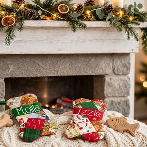 May include: Two bone-shaped fabric stockings featuring a colorful patchwork pattern of red, green, and white holiday motifs. One stocking is embroidered with the name Mollie in green, and the other with the name Izzie in white. Each has a hanging loop.