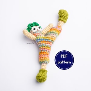 May include: A colorful crocheted amigurumi doll with green hair and large eyes, wearing a rainbow striped outfit. The doll is in a kicking pose with one leg raised. The image includes the text "PDF pattern".