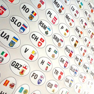 Peut inclure: Une collection d'autocollants ovales blancs avec des drapeaux de pays et leurs codes. Les autocollants, comme ceux de l'Italie, de la Suisse et de l'Ukraine, sont disposés en grille, créant un thème international.